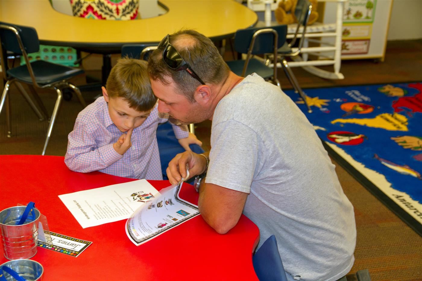 dad leaning on desk with elementary aged boy looking at information